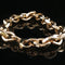 A chunky gold-toned chain link bracelet photographed on a glossy black reflective surface.
