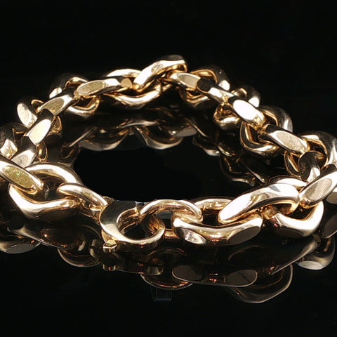 A chunky gold-toned chain link bracelet photographed on a glossy black reflective surface.