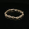 A gold chain link bracelet with a polished finish, displayed on a reflective black surface.