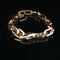 A chunky gold chain link bracelet with a lobster clasp, displayed on a reflective black surface.